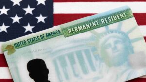 Primer plano de una Tarjeta de Residente Permanente de EE. UU. (Green Card) colocada sobre la bandera estadounidense, simbolizando la inmigración y la residencia permanente en Estados Unidos.